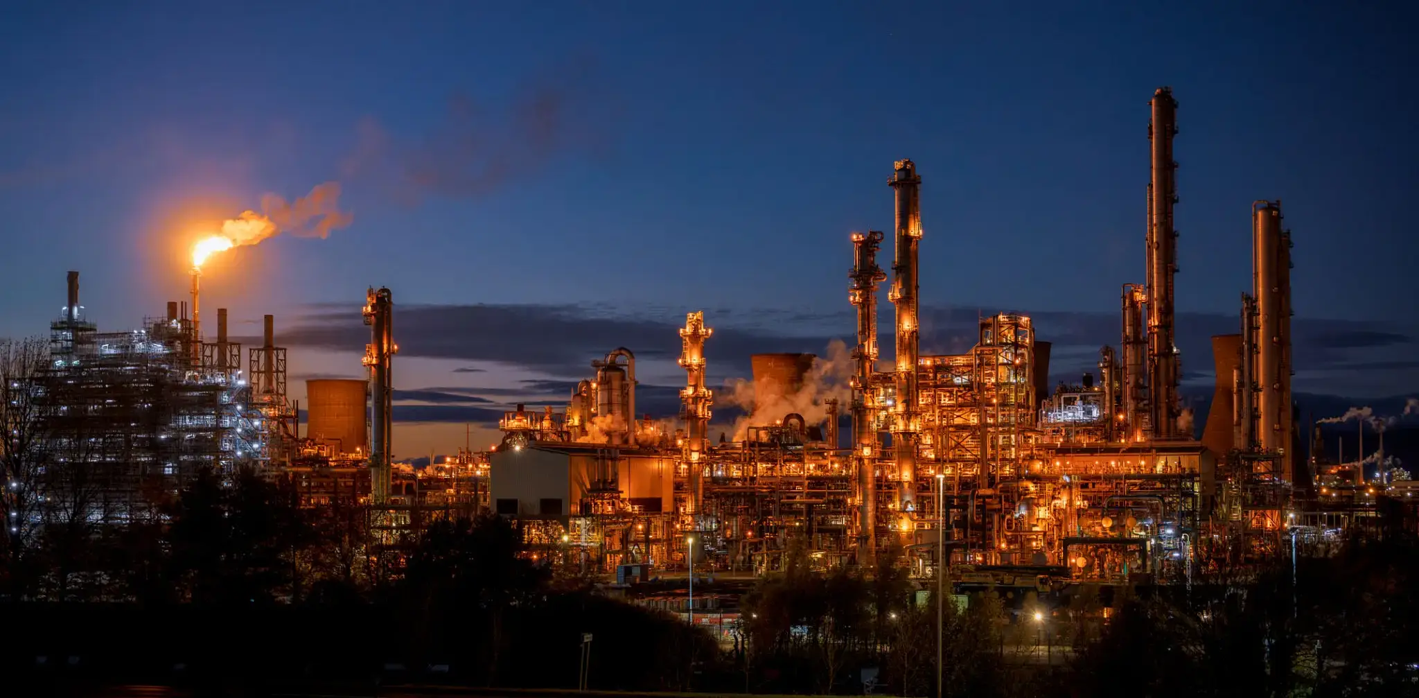 Industrial refinery lit up against the evening sky.