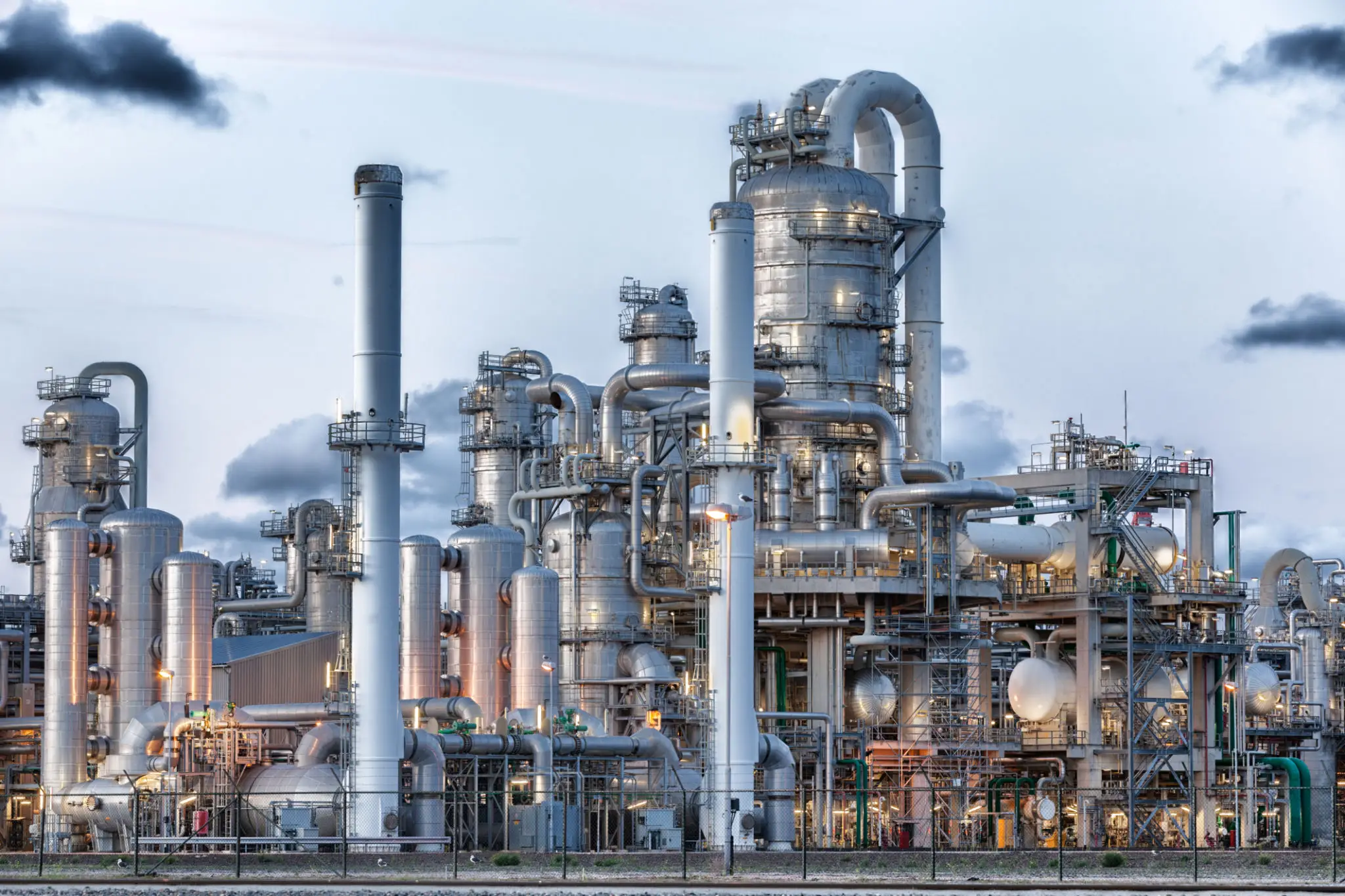 Large industrial refinery with complex piping and towers under a cloudy sky.